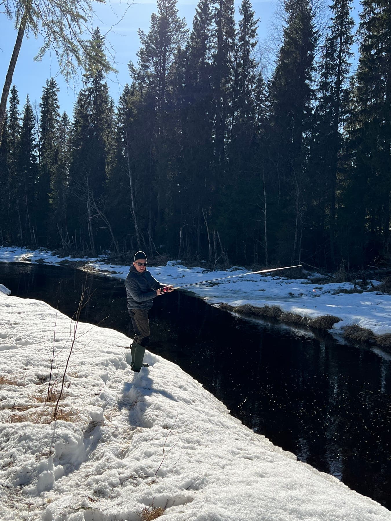Person kastar med spinnspö i öppen å som skär genom snötäcket