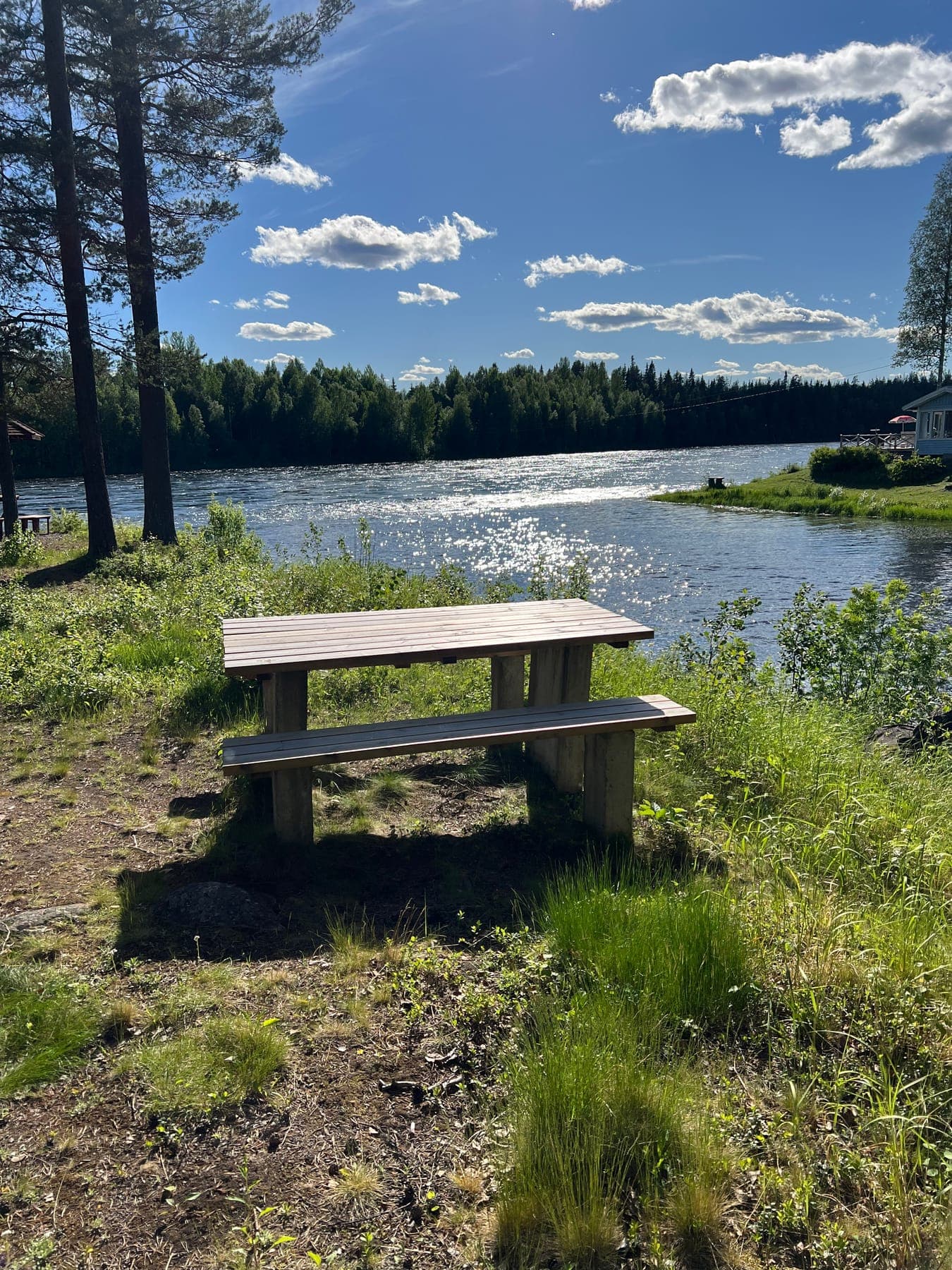 Picknickbord på strandbrink vid bred solglittrande älv