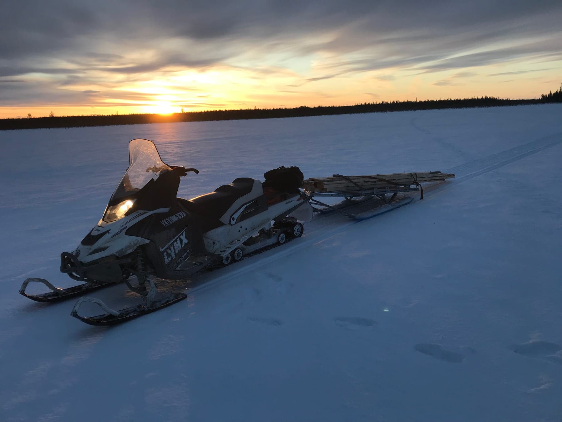Snöskoter med fullastad lastsläde på snötäckt myr i solnedgång